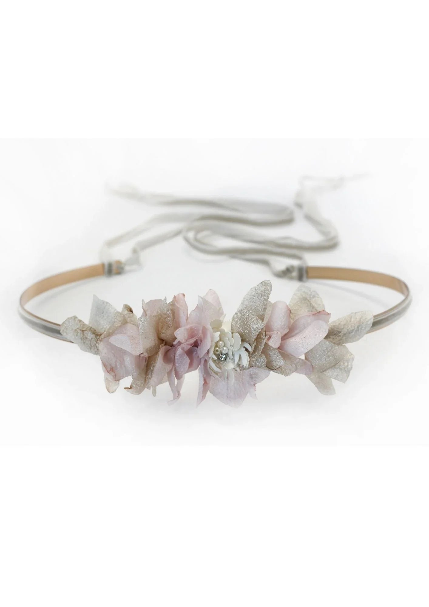 The CINTURÓN IBY is a delicate headband with soft pink and light beige artificial flowers and leaves, finished with thin ties at the back, from nuestra colección diseñada en España, shown on a white background.