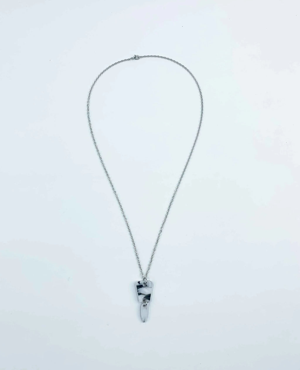 El Collar Minimalista de Cadena Plateada con Colgante Abstracto luce elegante con su diseño marmoleado y un aro transparente, ejemplificando la belleza de los collares artesanales. Destaca como una de nuestras auténticas joyas únicas sobre fondo blanco.