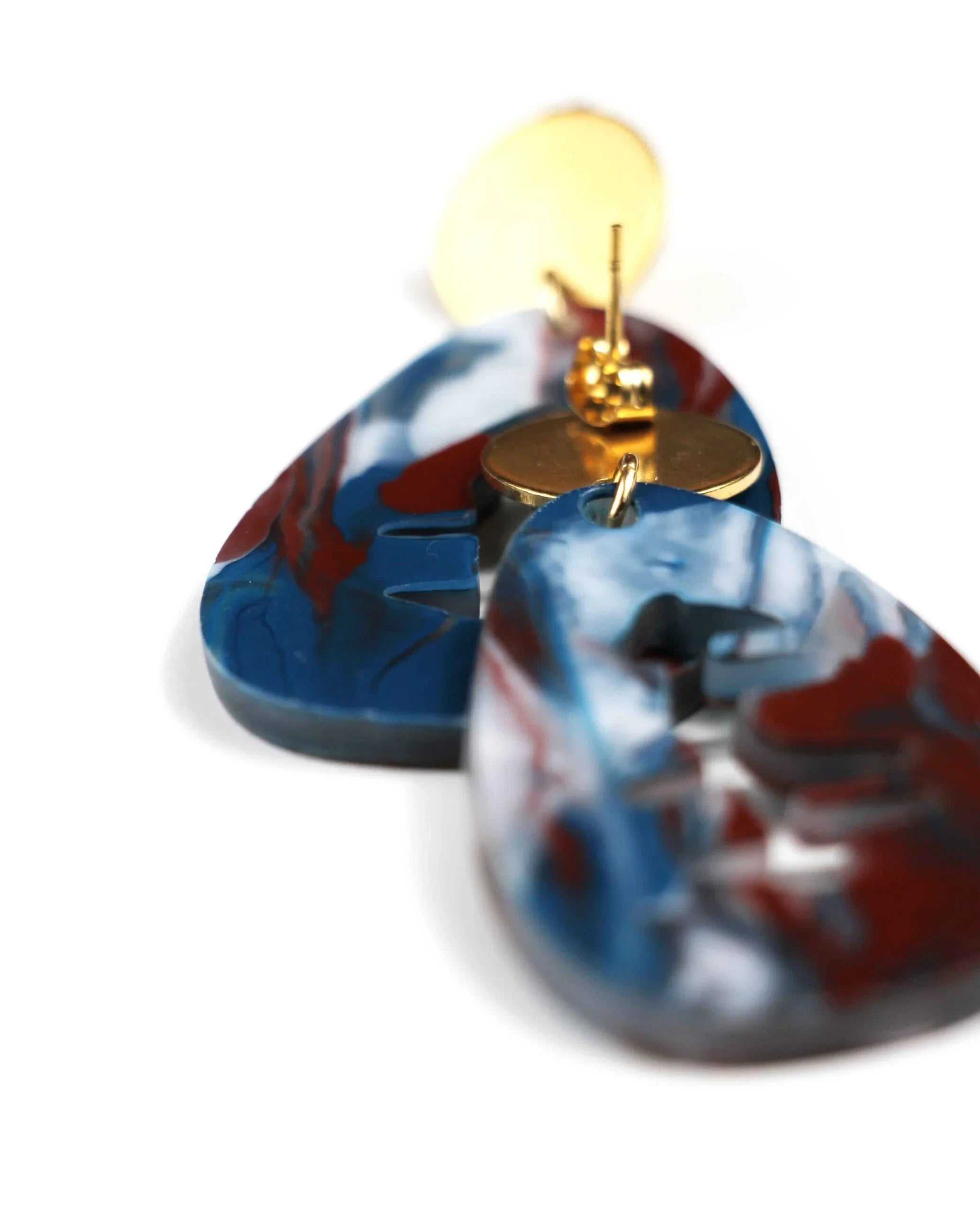 Close-up of Pendientes mármol marrón, azul, blanco y dorado: Accesorios inspirados en el amanecer con aros dorados y colgantes de resina marmoleada. Fondo blanco.